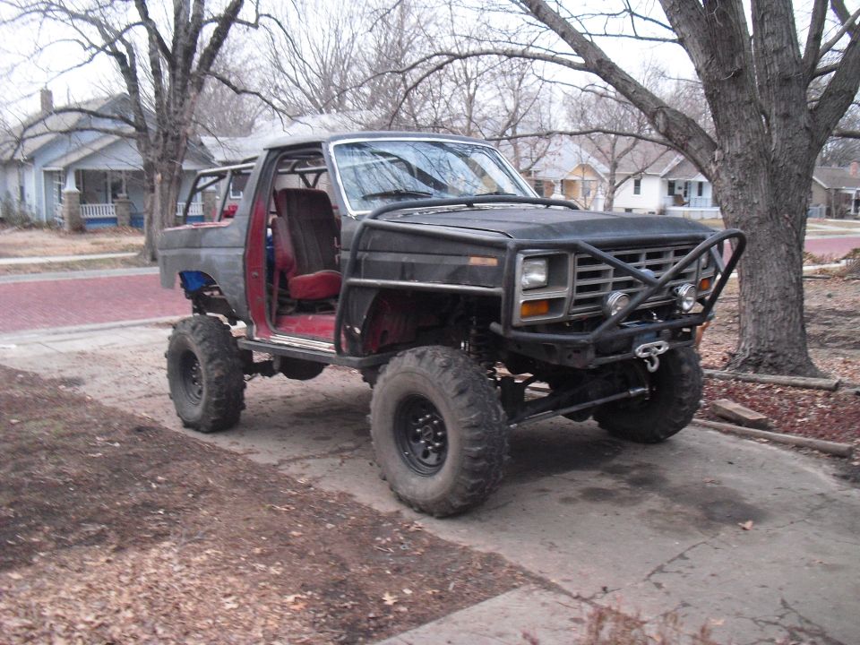 Black modified Ford Bronco with off-road tires, roll cage, and custom bumper