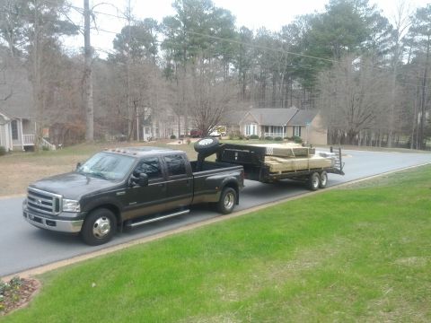 1979 Ford F-150 - A dually pickup truck tows a trailer filled with lumber down a suburban street.