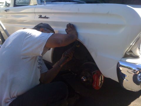 1964 Ford Ranchero - Mechanic works on the front fender of a white 1964 Ford Ranchero, revealing red brake calipers.