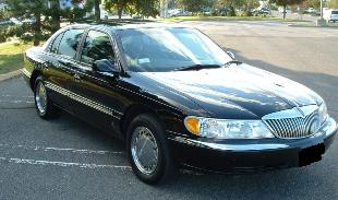1997 Ford Crown Victoria - This black sedan is parked in an asphalt lot with trees in the background.