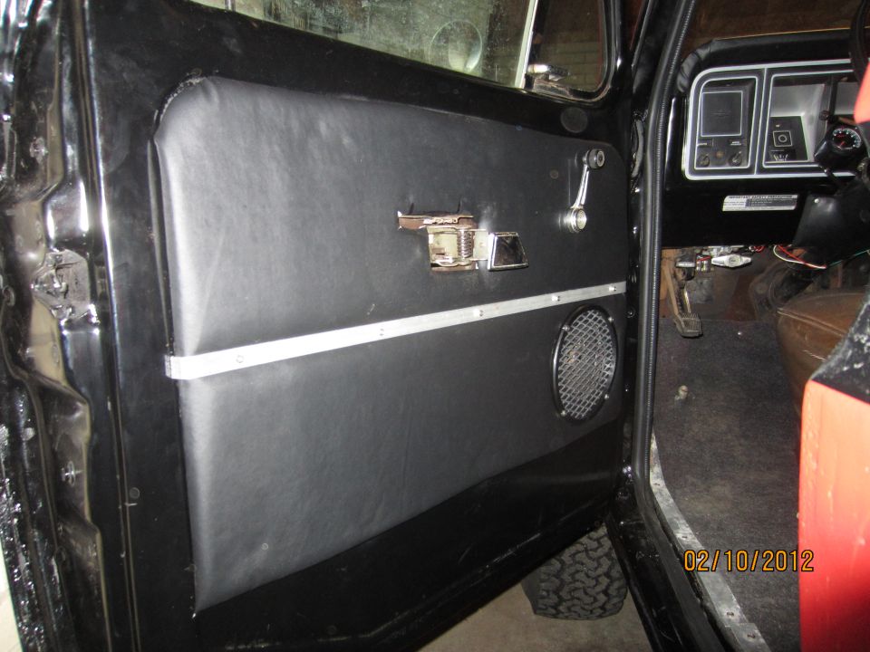 Interior shot of a vehicle door panel with a speaker and chrome handle, showing part of the dashboard and steering wheel