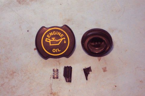 1996 Ford Bronco - Disassembled engine oil cap and associated components laid out on a textured surface.