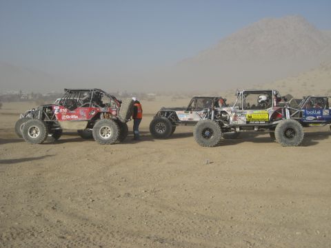 1996 Ford Bronco - Off-road vehicles are parked in a dusty desert environment, with a person standing between them.