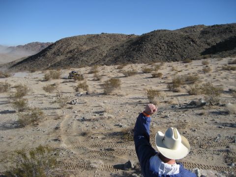 1996 Ford Bronco - A person in a cowboy hat points towards an off-road vehicle in a dusty desert environment.