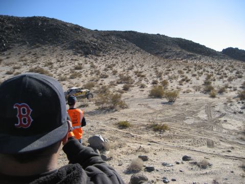 1996 Ford Bronco - Two people watch an off-road buggy navigate a dusty desert terrain under a clear blue sky.