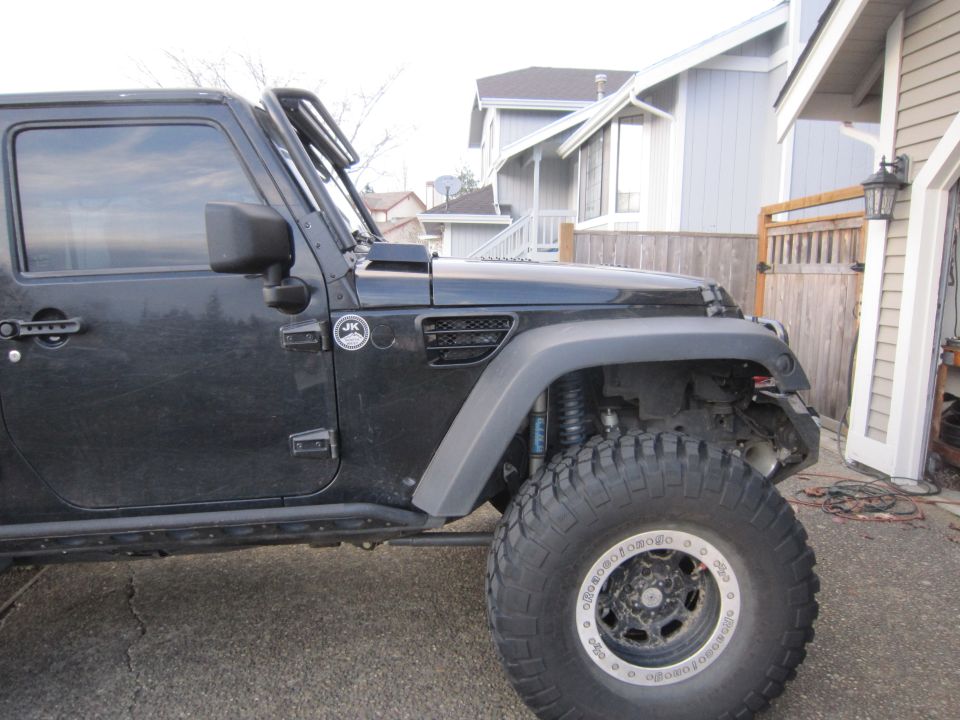 Black Jeep Wrangler with large off-road tire and custom fender vent. "JK" badge visible