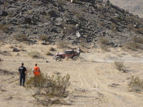 1996 Ford Bronco - A red off-road buggy navigates a dusty desert course with two spectators watching.