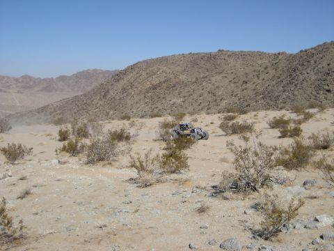 1996 Ford Bronco - An off-road buggy navigates a dry, desert terrain under a clear blue sky.