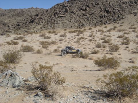 1996 Ford Bronco - A custom off-road buggy navigates a sandy, arid terrain under a clear blue sky.