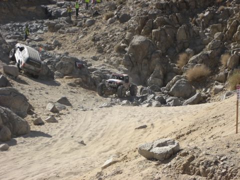 1996 Ford Bronco - Two off-road vehicles compete in a desert race, navigating a challenging rocky and sandy course.