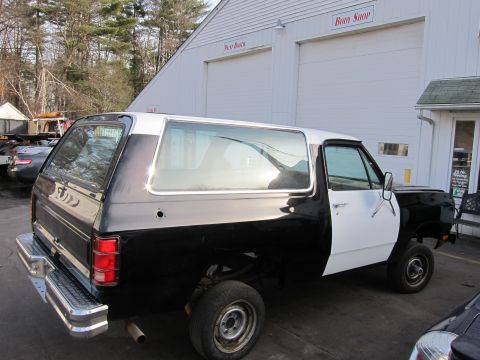 1987 Dodge 1500 - A two-tone Dodge Ramcharger is parked outside a body shop, showing its side profile and rear quarter panel.