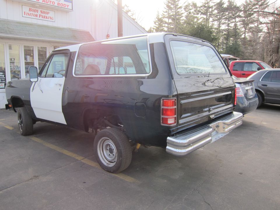 Two-tone Dodge Ramcharger with black rear and white front, parked outside a body shop