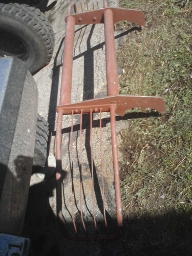 1989 Ford Bronco - A close-up view of a rusted agricultural implement with multiple tines, partially obscured by a vehicle tire.
