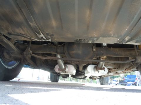 1982 Chevrolet Camaro - The underside of a car reveals its rear axle, dual exhaust, and fuel tank, with a truck in the distance.