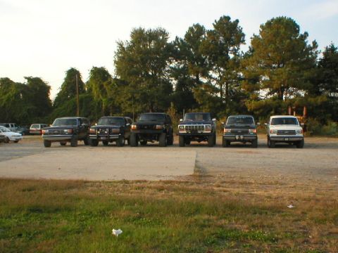 1989 Ford Bronco - Several SUVs and trucks are parked in a line, viewed from the front. One vehicle resembles a 1989 Ford Bronco.