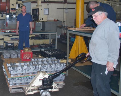 1969 Ford Fairlane - Workers in a factory move large quantities of engine cylinder heads on pallets.