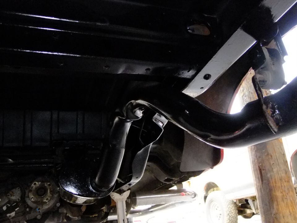 Underside view of a vehicle's rear suspension and exhaust system, painted black