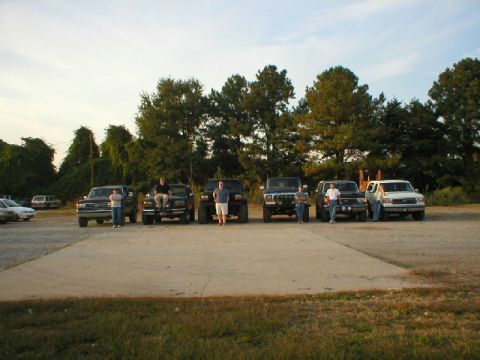 1989 Ford Bronco - A group of trucks and SUVs are parked together outdoors on a sunny day.
