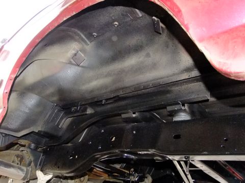 1995 Ford Bronco - Close-up view of the rear chassis and wheel well of a red vehicle, highlighting the undercoating.