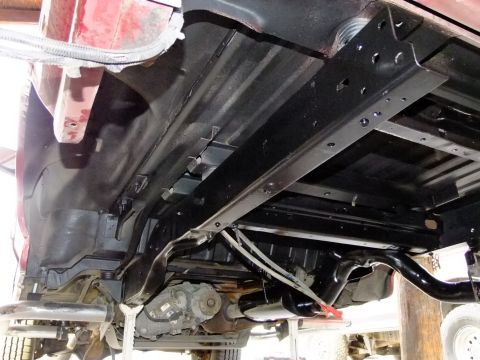 1995 Ford Bronco - Underside view of a red 1995 Ford Bronco's rear chassis, detailing the frame, exhaust system, and transfer case.