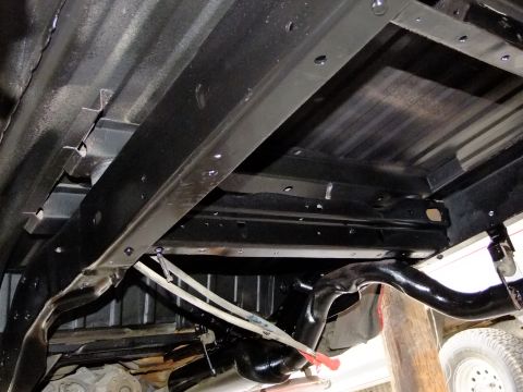 1995 Ford Bronco - The underside of a vehicle shows black painted frame rails and suspension parts.