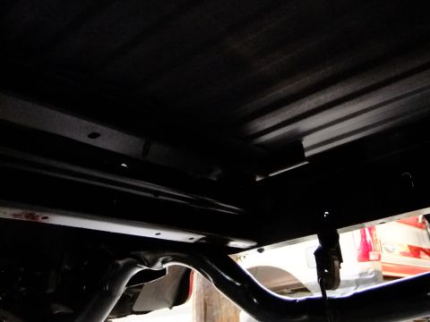 1995 Ford Bronco - The underside of a vehicle is shown, with focus on the frame and suspension parts. Another vehicle's taillight is visible.