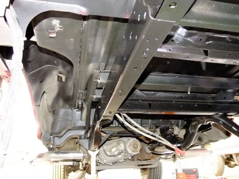 Underside of a vehicle showing the chassis, drivetrain components, and exhaust system
