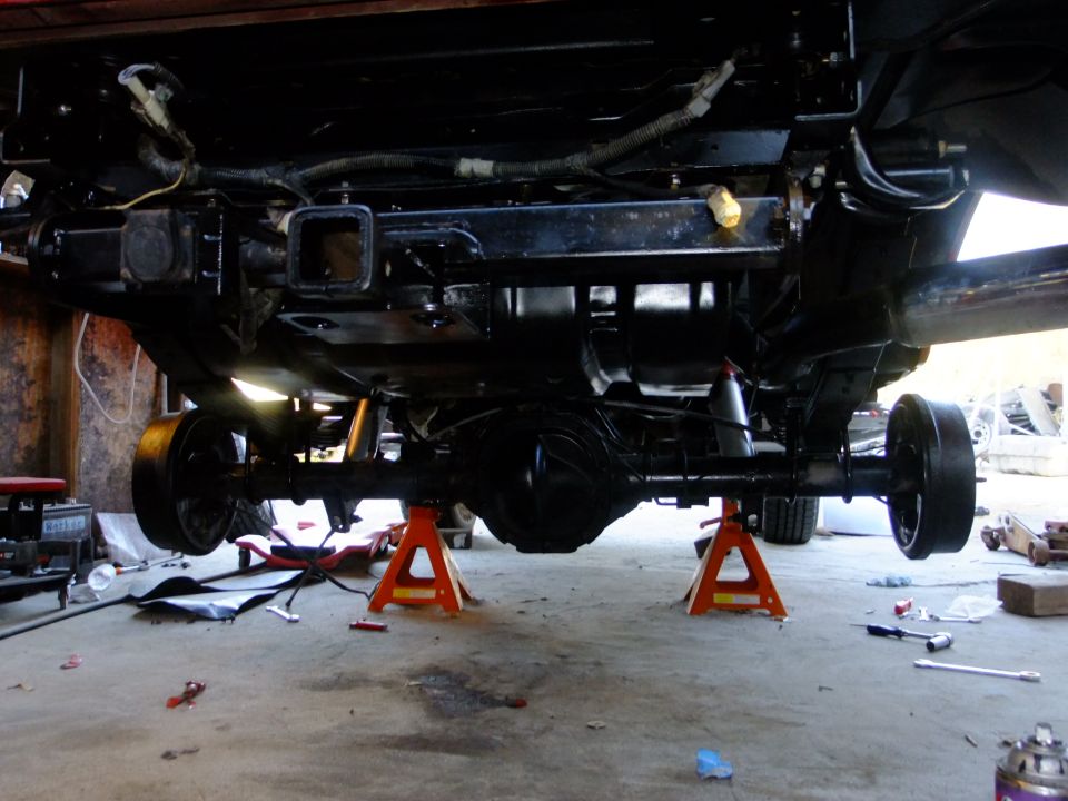 Underside of a vehicle on jack stands, showing the rear axle, suspension, and hitch receiver