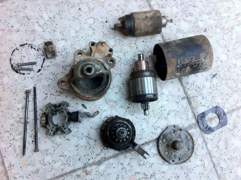1998 Ford Crown Victoria - Starter motor components are disassembled and spread out on a patterned floor.