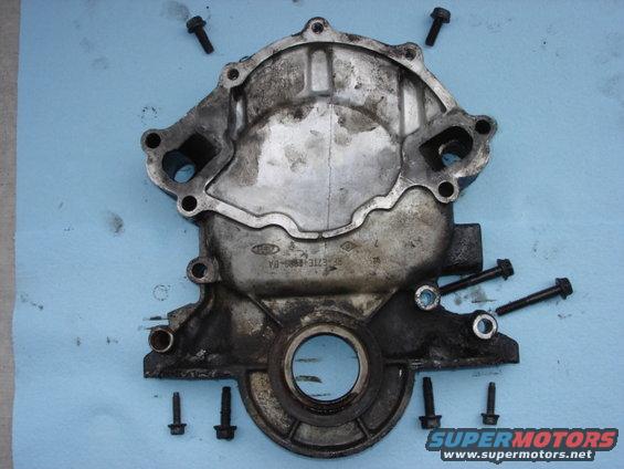 Dirty metal engine timing cover with Ford logo and part number visible, surrounded by bolts on a blue cloth