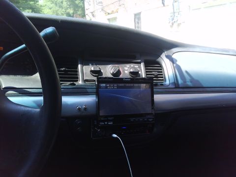 1999 Ford Crown Victoria - The dashboard of a car shows an aftermarket stereo system with a touchscreen display and visible controls.
