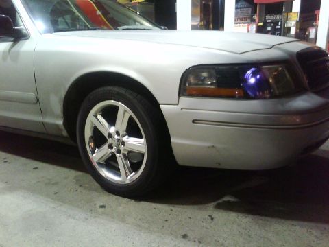 1999 Ford Crown Victoria - Front quarter panel and wheel of a silver Ford Crown Victoria, showing custom headlights.