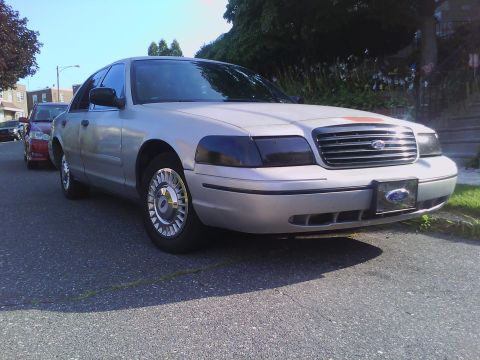 1999 Ford Crown Victoria - A silver Ford Crown Victoria is parked on the street, with a red car behind it.
