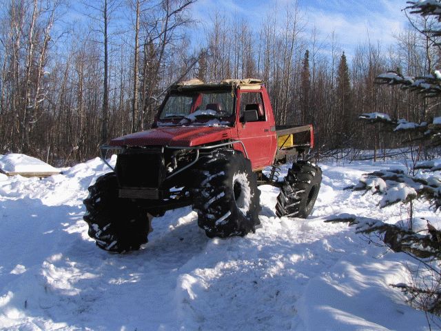 Red Suzuki Samurai pickup truck with large tires in a snowy forest.