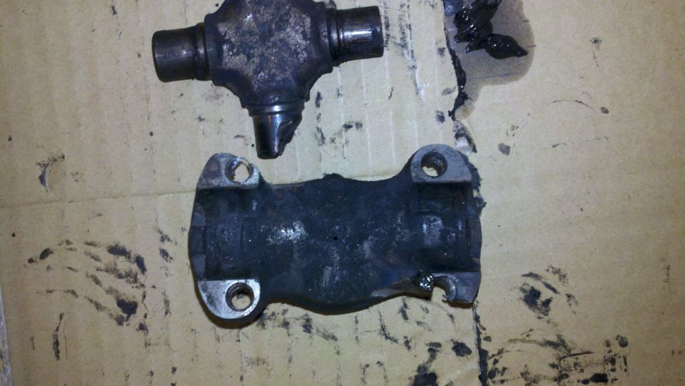 Two greasy driveshaft universal joint parts on a cardboard surface