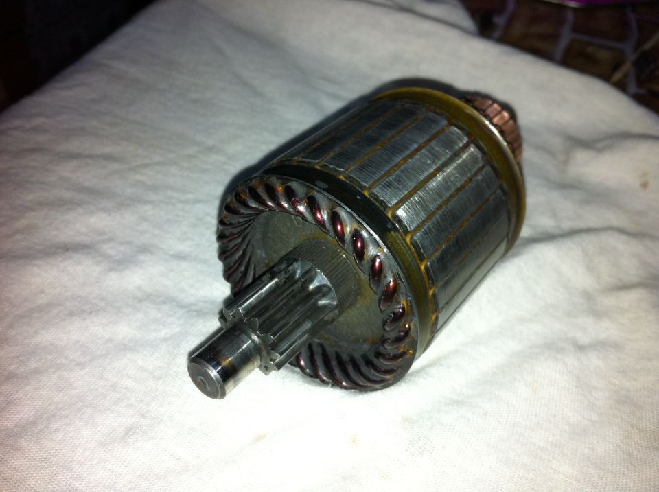 Starter motor armature with copper windings and a splined shaft, resting on a white cloth
