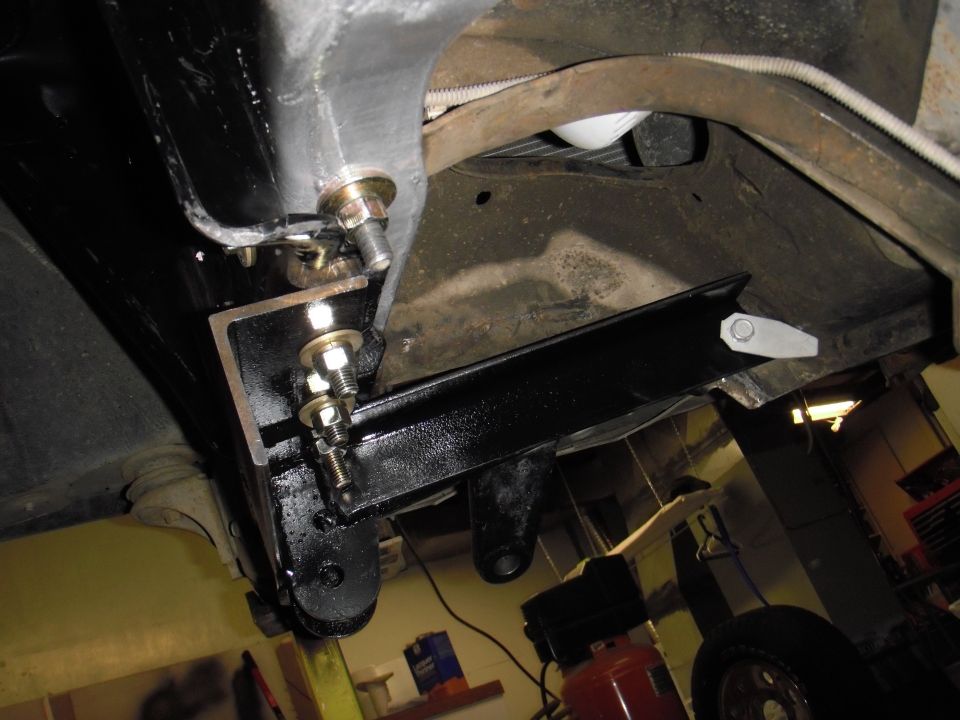 Underside of a vehicle showing black aftermarket brackets bolted to the frame, with some suspension components visible