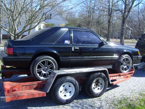 2007 Ford Mustang - This black coupe, likely a Fox Body Mustang from the late 1980s, is seen loaded onto a U-Haul trailer.