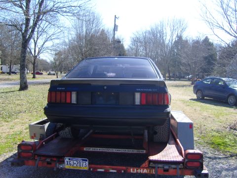 2007 Ford Mustang - A dark blue Ford Mustang is loaded onto a U-Haul trailer, with another car visible in the background.