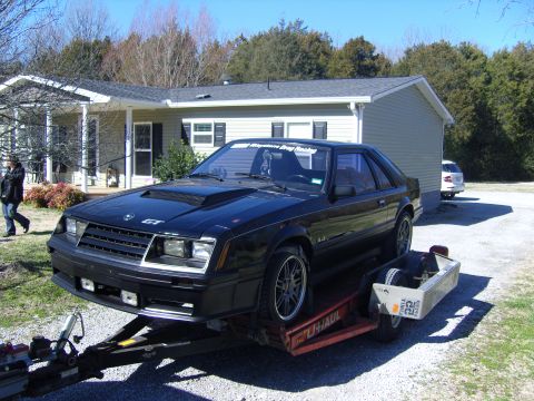 2007 Ford Mustang - A black Ford Mustang GT is loaded onto a trailer in front of a house.