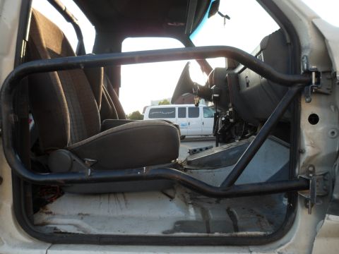 1991 Ford Bronco - The interior of a vehicle shows a roll cage and seats, with a white van in the background.