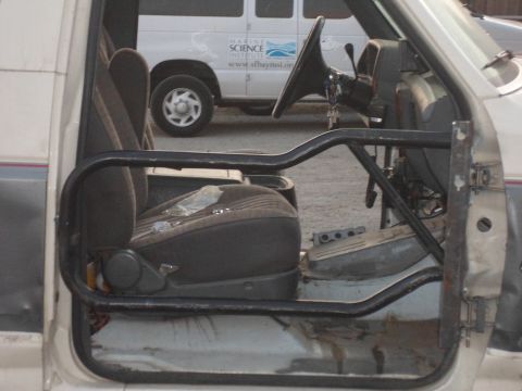 1991 Ford Bronco - The interior of a vehicle is shown, a roll cage and a view of a van in the background.