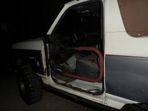 1991 Ford Bronco - The interior of a white Ford Bronco is visible with the driver's side door open, revealing a red roll bar.
