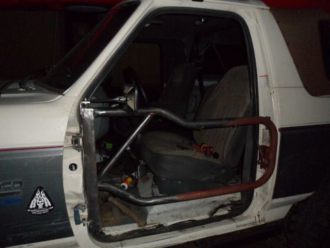 1991 Ford Bronco - The interior of a white Ford Bronco, showing the driver's seat and a custom roll cage installed.