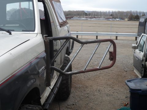 1991 Ford Bronco - A custom-fabricated off-road door is attached to the side of a white and dark gray SUV, with another vehicle visible to the right.