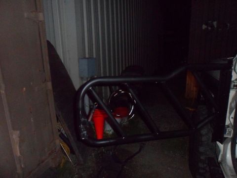 1991 Ford Bronco - A black roll cage is attached to a vehicle, with a red taillight and an orange cone visible.