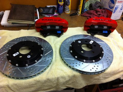 2010 Dodge Challenger - A pair of red BAER brake calipers and two drilled brake rotors are laid out on a towel on a workbench.