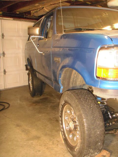 1995 Ford Bronco - A blue SUV is parked inside a garage, showing its front quarter panel and wheel.