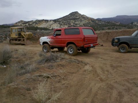 1979 Ford Bronco - Red and white Ford Bronco with flame decals on a dirt road, with a bulldozer and another SUV nearby.