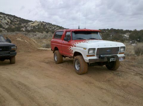 1979 Ford Bronco - A red and white Ford Bronco with flame decals is parked on a dirt road, with another vehicle visible to the left.